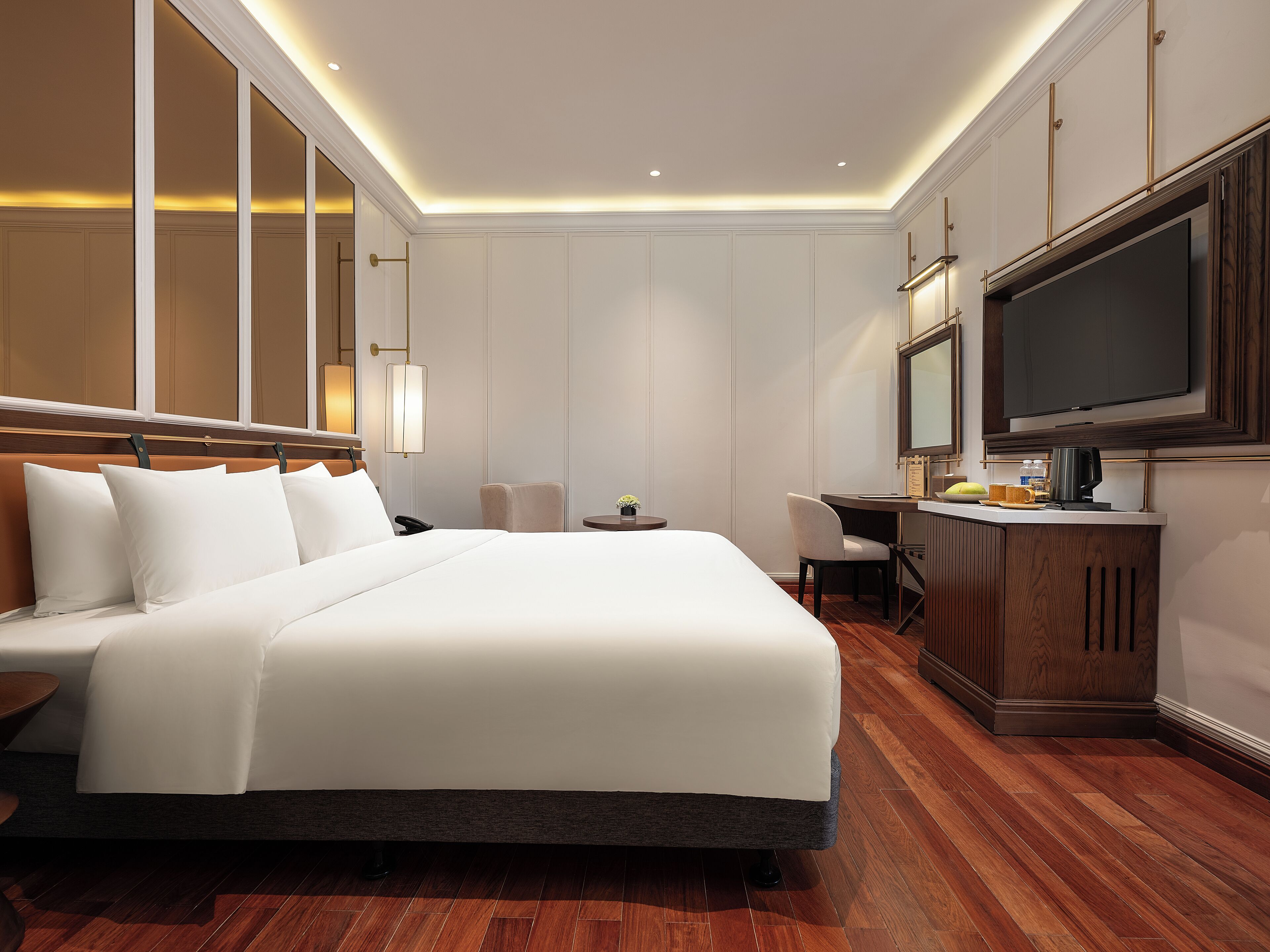 A hotel room with a large bed, a desk with a chair, a television, and a minibar.