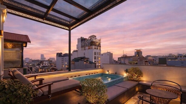 Eine Dachterrasse mit Pool, Liegestühlen und Blick auf die Skyline im Abendlicht.