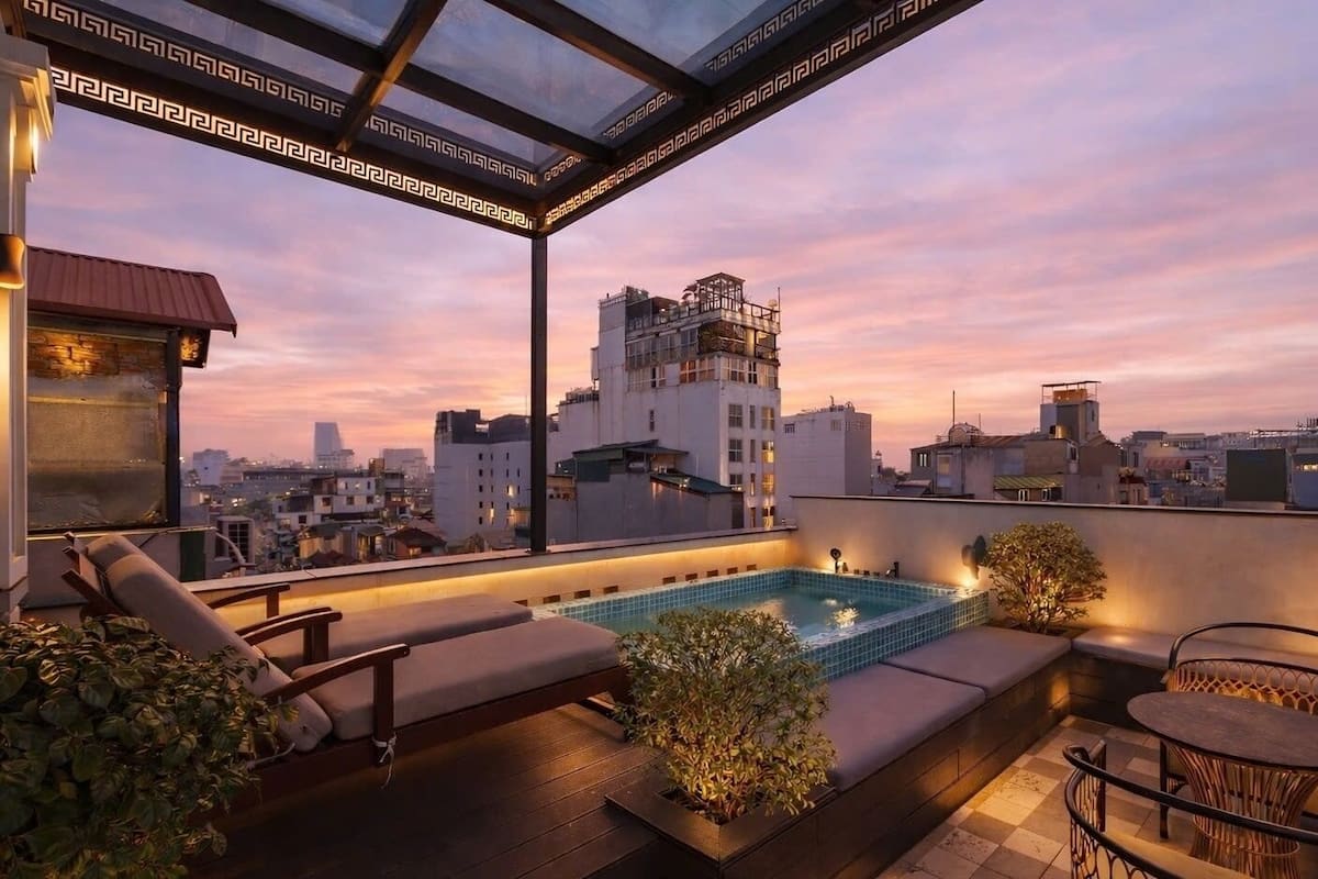 A rooftop terrace with a swimming pool, lounge chairs, and a view of the cityscape at sunset.