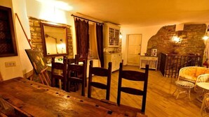A rustic dining area with a wooden table and chairs, a stone wall, and a cozy seating area with a cushioned chair. - Il Borgo del Castello Large Double Room Tulip (Cremolino)