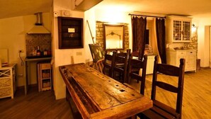 A rustic dining area with a wooden table and chairs, a stone fireplace, and a kitchen area with cabinets and a sink. - Il Borgo del Castello Large Double Room Tulip (Cremolino)