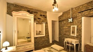 A bedroom with a stone wall, a large mirror, a bedside table, and a bed with a patterned bedspread. - Il Borgo del Castello Large Double Room Tulip (Cremolino)