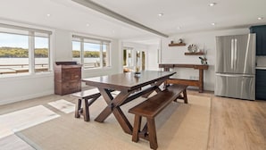 Une cuisine moderne dotée d’une grande table en bois, d’appareils électroménagers intégrés et de grandes fenêtres offrant une vue panoramique.