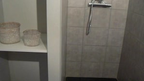 A small bathroom with a shower, a toilet, and a shelf with two containers.