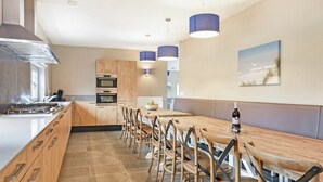 Una cocina moderna con armarios de madera, horno empotrado, campana extractora de acero inoxidable y una larga mesa de comedor con sillas de madera.