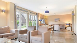 Amplia sala de estar con una mesa de comedor, asientos cómodos y ventanas grandes que ofrecen vistas al exterior.