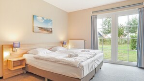 Habitación de hotel con una cama grande, dos mesitas de noche con lámparas, un cuadro en la pared y vistas amplias por un ventanal.