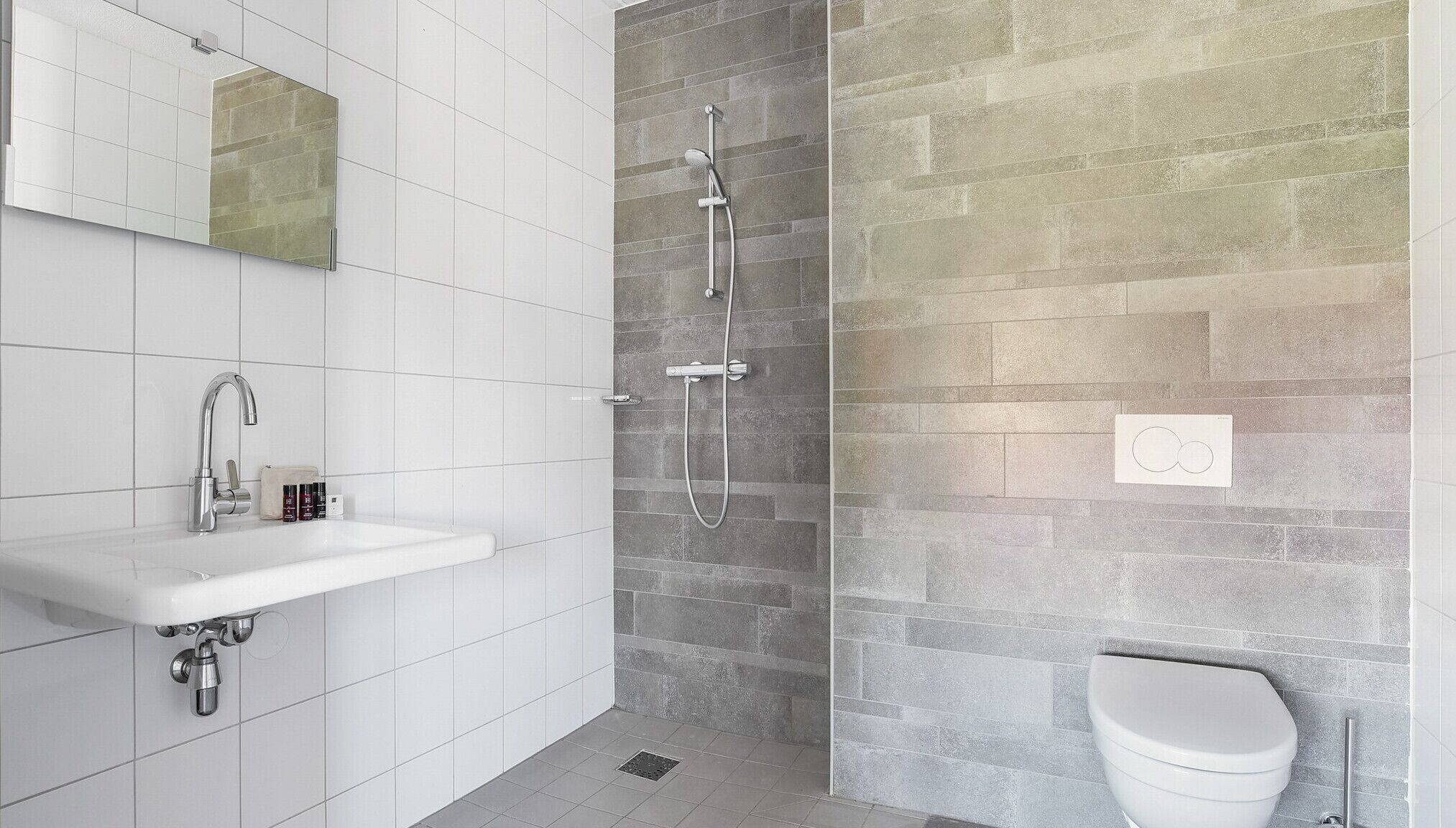 Ein modernes Badezimmer mit einem weißen Waschbecken, einer Dusche mit Duschhandstück und einer Toilette.