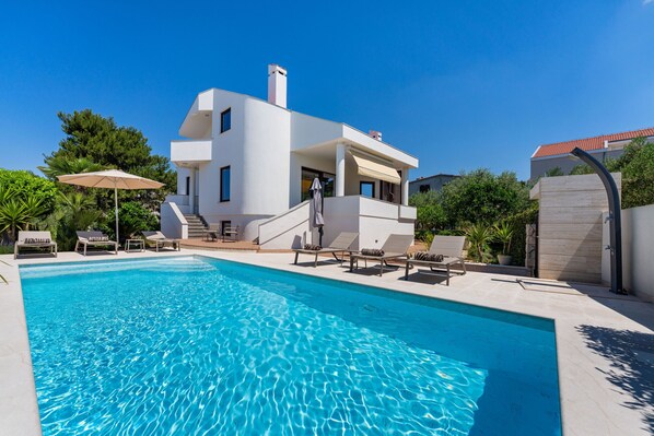 A modern two-story house with a swimming pool, outdoor lounge chairs, and a covered patio area.