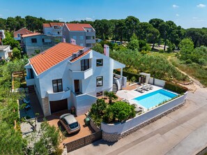 A modern two-story house with a swimming pool, a car parked in the driveway, and a view of the surrounding landscape.