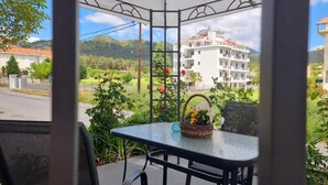 Un espacio de estar al aire libre con techo, con una mesa y sillas, con vista a una zona residencial con edificios y vegetación.