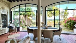 Une pièce dotée d’une grande porte vitrée donnant sur un jardin, d’une table ronde avec des chaises, d’un canapé et d’un meuble avec des portes vitrées.