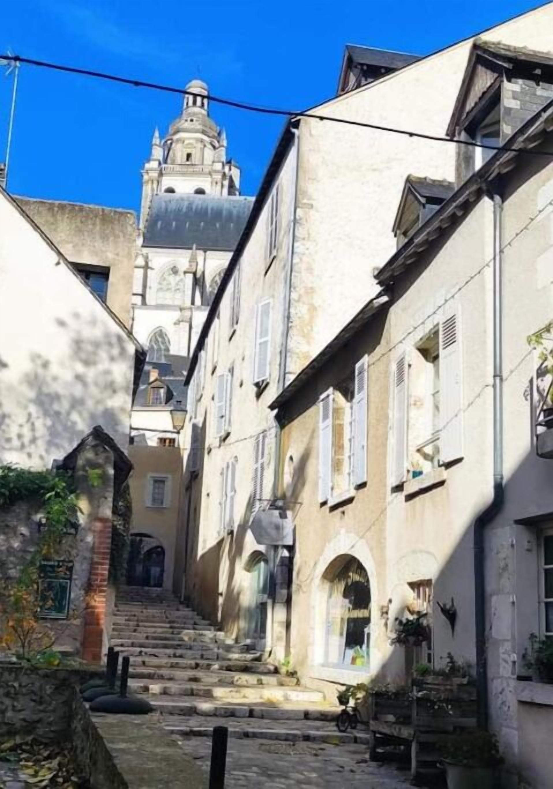 Une rue étroite avec des marches en pierre menant à un bâtiment surmonté d’un clocher.