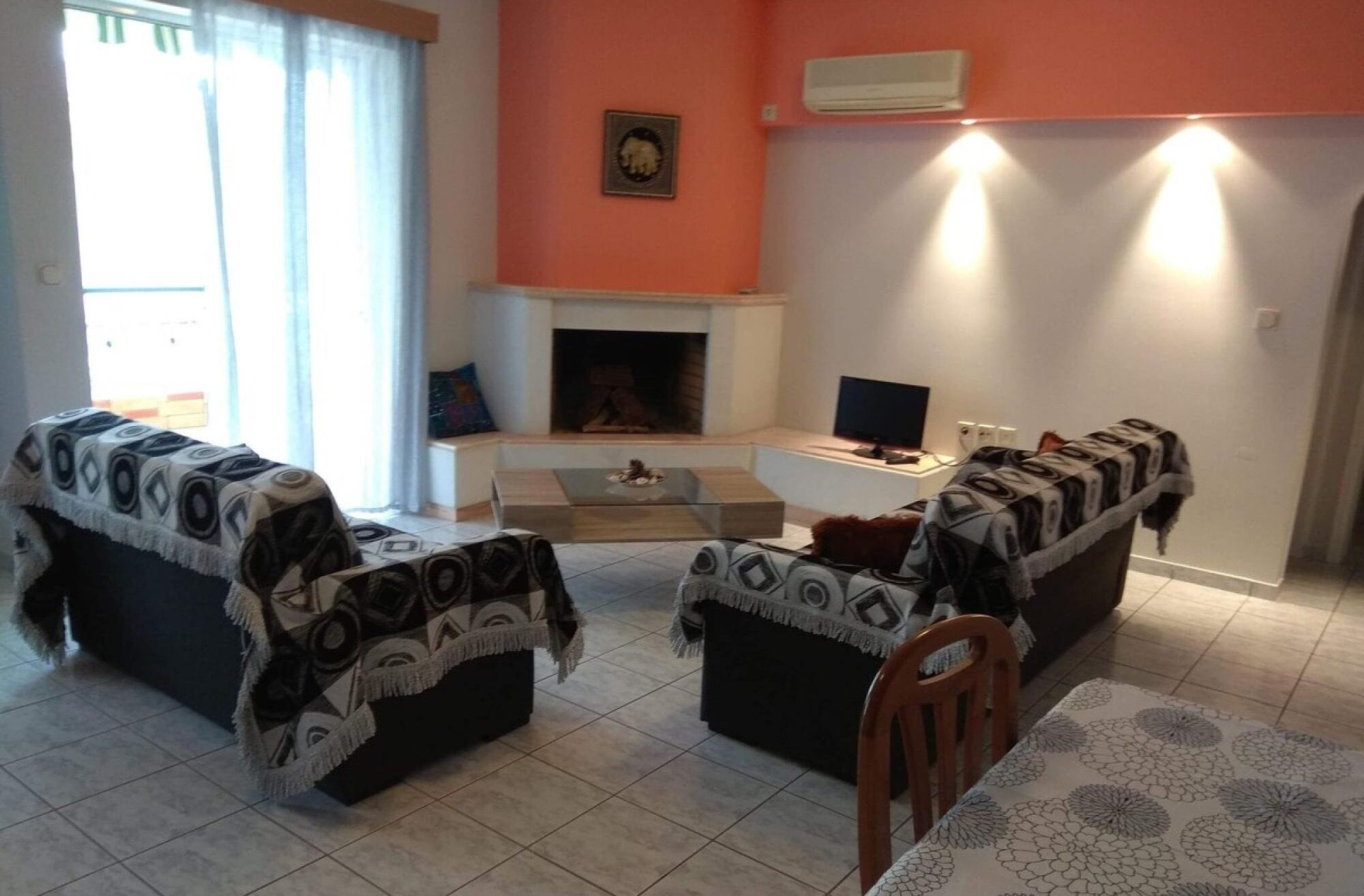 A living room with two sofas covered with patterned blankets, a fireplace, a television, and a dining table with a patterned tablecloth.