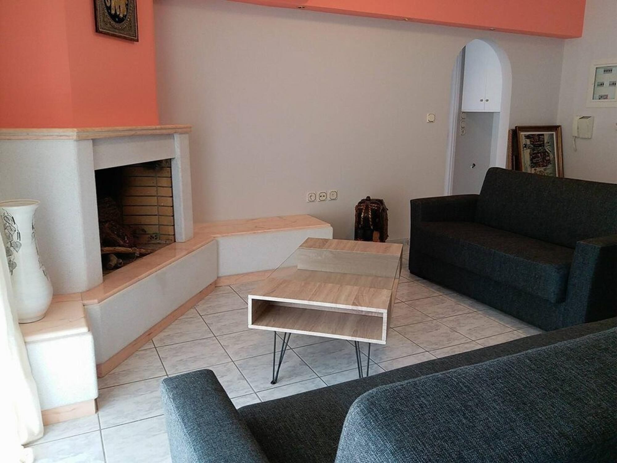 A living room with a fireplace, a dark grey sofa, a white coffee table, and a tiled floor.