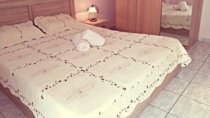 A neatly made bed with a floral-patterned bedspread, a rolled towel, and a bedside lamp. - Daphnus Apartment in Agios Konstantinos (Kamena Vourla)