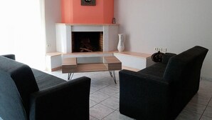 A living room with a fireplace, two black sofas, a white vase, and a framed picture on the wall. - Daphnus Apartment in Agios Konstantinos (Kamena Vourla)