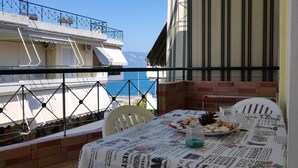 A balcony with a table set for dining, overlooking a coastal view. - Daphnus Apartment in Agios Konstantinos (Kamena Vourla)