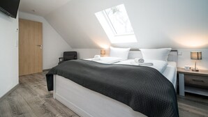 A modern bedroom with a skylight, a bed with a dark blanket, bedside tables with lamps, and a wooden door. - Ferienhaus Nationalparkidylle in Boek (Rechlin)