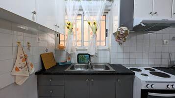 Une cuisine avec des meubles blancs, une cuisinière, un évier et une fenêtre avec un rideau.