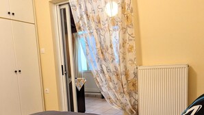 A bedroom with a bed, two rolled towels, a radiator, and a door with a curtain. - Central Apartment in Agios Konstantinos (Kamena Vourla)
