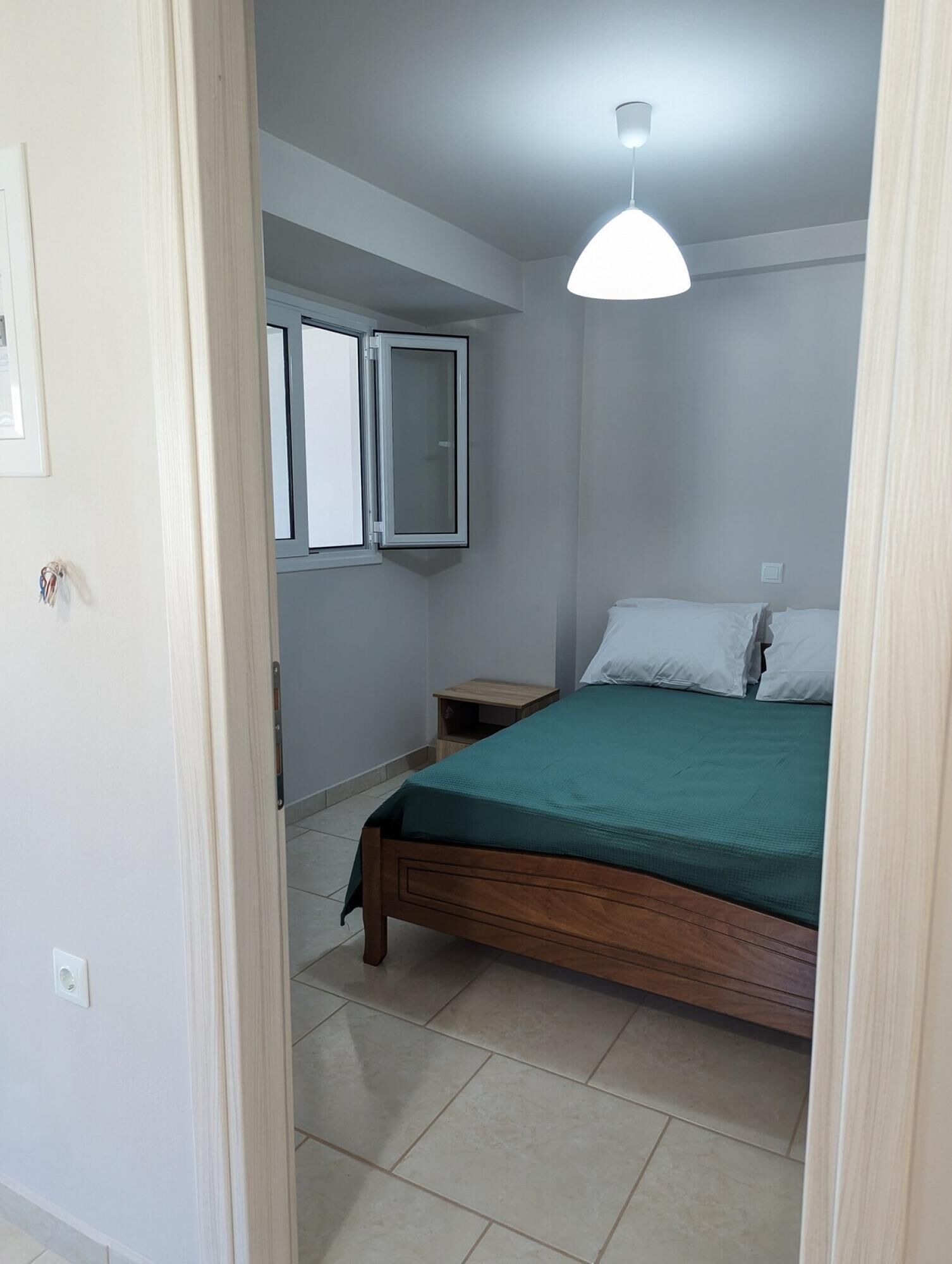 Un dormitorio con cama, mesita de noche, ventana y lámpara de techo.