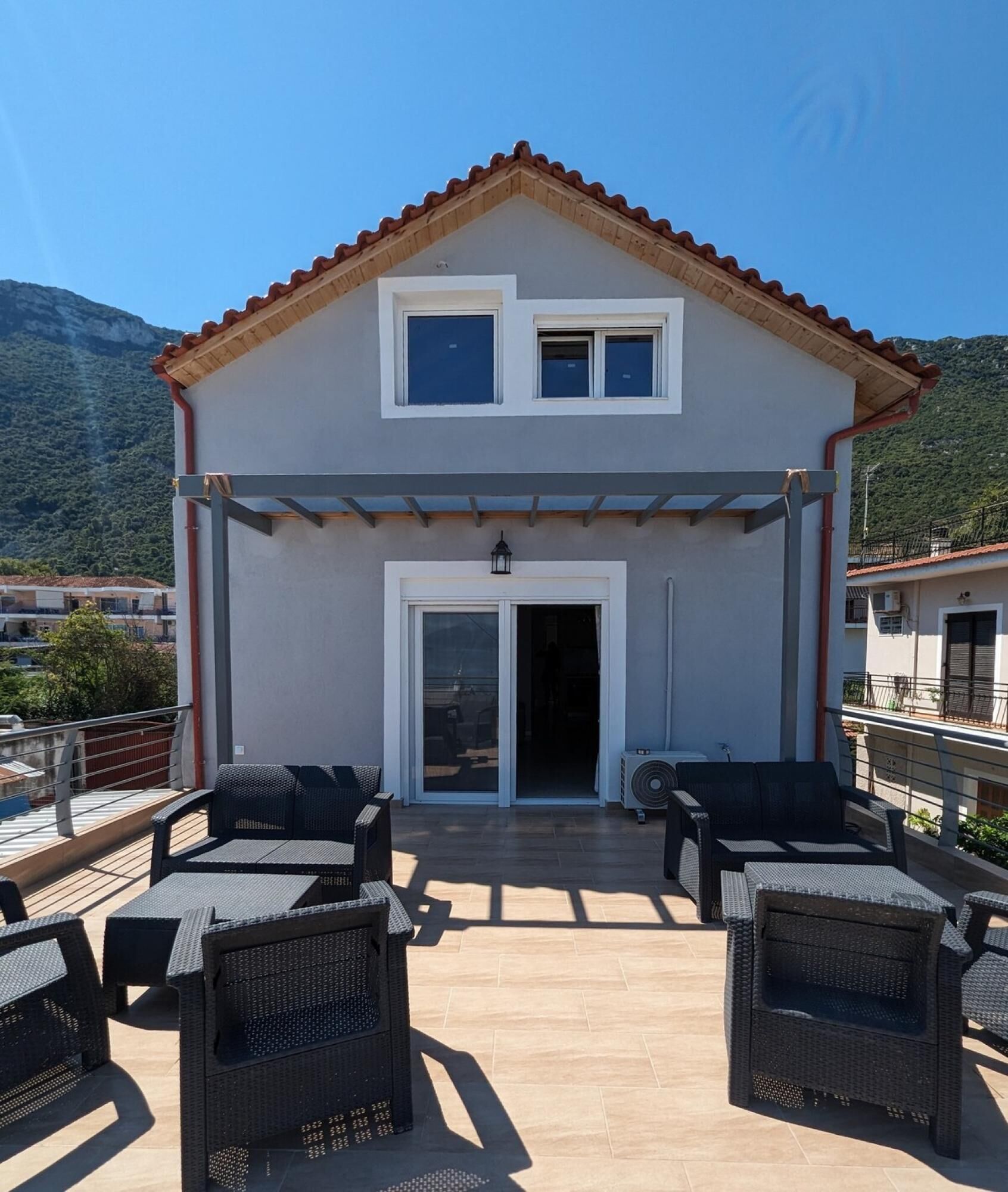 Ein zweistöckiges Gebäude mit einer gefliesten Terrasse und Gartenmöbeln.