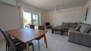 A spacious living room with a wooden dining table, grey sofa, and a TV on a stand. - Bella Vista Luxury Apartment (Kamena Vourla)