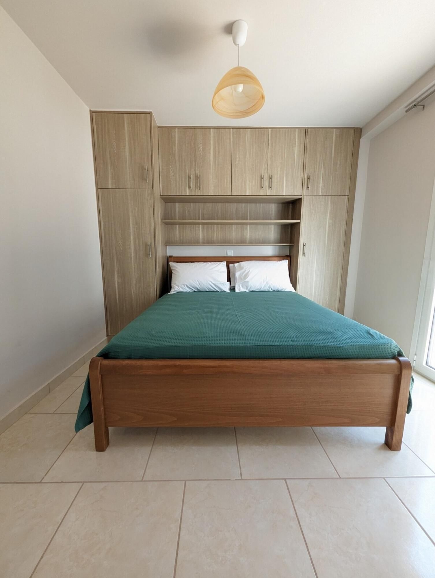 A bedroom with a wooden bed, a green bedspread, and light wooden cabinetry.