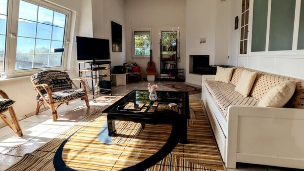 Una sala de estar con un sofá, sillones, una mesa de centro, un televisor y una estantería.