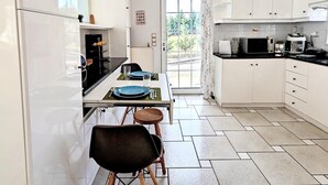 Una cocina moderna con armarios blancos, una mesa de comedor para dos personas y un ventanal que proporciona luz natural.
