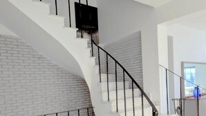Una escalera moderna con escalones blancos y barandillas negras, que conduce a un rellano con un muro de ladrillo y una puerta.