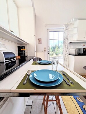 A modern kitchen with white cabinets, a black countertop, and a dining area set with blue plates, silverware, and a glass. - Ecoscape Luxury Villa Lamia (Lamia)