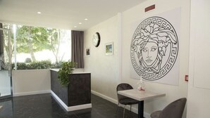 A reception area with a marble floor, a reception desk, two chairs, a clock, and a large wall art piece. - B&B Laura (Terzigno)