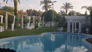 A swimming pool with a curved edge, surrounded by white outdoor furniture and a pergola. - B&B Laura (Terzigno)