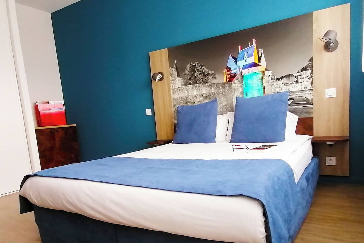 Ein Schlafzimmer mit einem Bett, einem Nachttisch, einer Wandlampe und einem roten Gegenstand auf einem Holzkasten.