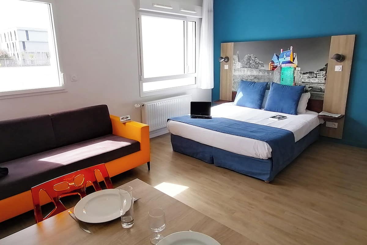Ein Zimmer mit einem Bett, einem Sofa, einem Tisch mit Tellern und Gläsern sowie einem Laptop auf dem Bett.
