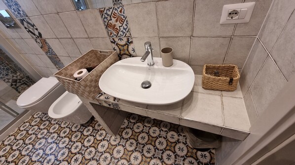 A bathroom with a toilet, a sink with a mirror, and a patterned floor. - B&B Arcovito 36 (Reggio Calabria)