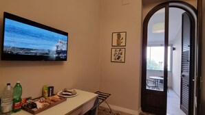 A room with a TV on the wall, a dining table with food and drinks, and a balcony with a door. - B&B Arcovito 36 (Reggio Calabria)