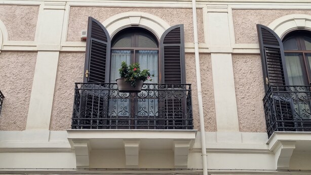A building facade with three arched windows, each with dark shutters and a potted plant on the balcony. - B&B Arcovito 36 (Reggio Calabria)