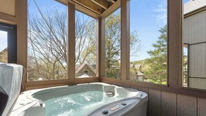 Un bain à remous dans une pièce aux murs en bois, dotée de grandes fenêtres.