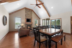 Un salón espacioso con chimenea, un comedor con una gran mesa de madera y un ventilador de techo.