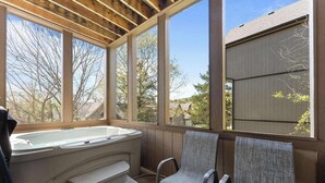 Un bain à remous avec des marches, deux fauteuils et de grandes fenêtres donnant sur les arbres et les maisons.