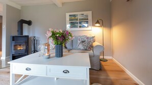 A modern living room with a white sofa, a decorative vase with flowers, a small table, and a fireplace. - Backbord- wood-burning stove,grill, shower, close to the beach, terrace, parking (Steinbergkirche)