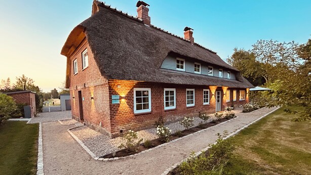 A two-story house with a thatched roof, a gravel driveway, and a well-maintained garden. - Backbord- wood-burning stove,grill, shower, close to the beach, terrace, parking (Steinbergkirche)