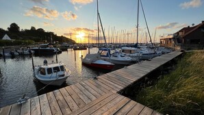 A marina with boats docked at wooden piers, a clear sky, and a sunset in the background. - Backbord- wood-burning stove,grill, shower, close to the beach, terrace, parking (Steinbergkirche)