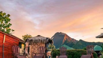 Een tropisch resort met houten stoelen en een hut met rieten dak, met een berg op de achtergrond.