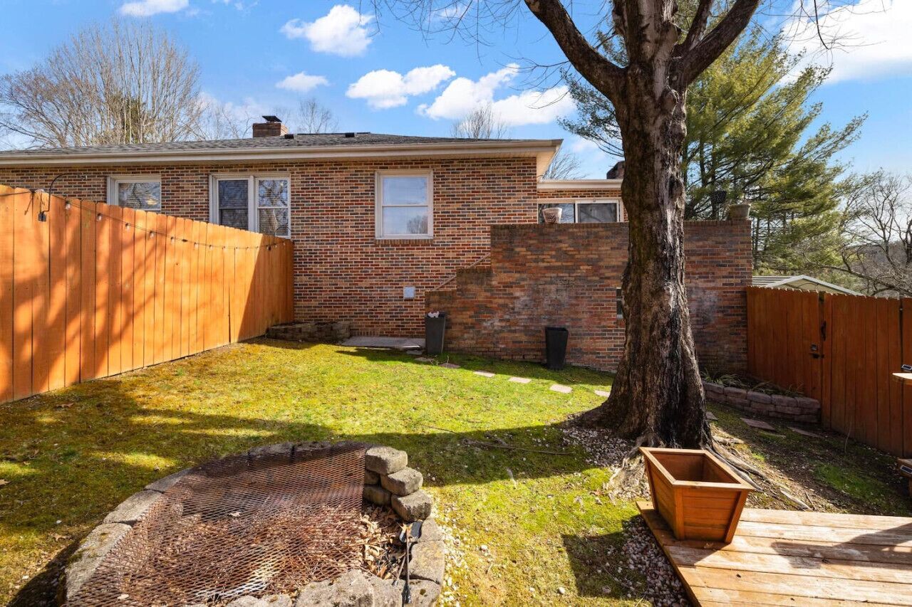 A brick house with a wooden fence, a tree, and a fire pit in the backyard.