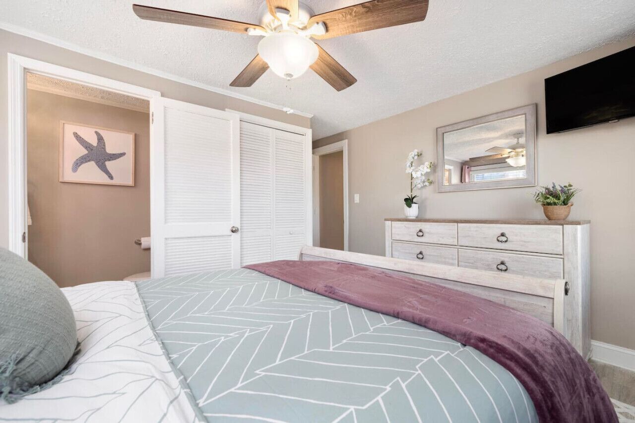 A bedroom with a bed, a ceiling fan, a dresser, a mirror, and a starfish decoration.