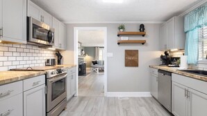 A modern kitchen with white cabinets, stainless steel appliances, and a wooden countertop. There are two hanging shelves with decorative items and a sign on the wall.
